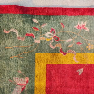 A corner of a green floral rug framed by thick borders in vivid red and golden yellow.