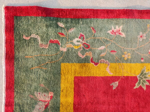 A corner of a green floral rug framed by thick borders in vivid red and golden yellow.