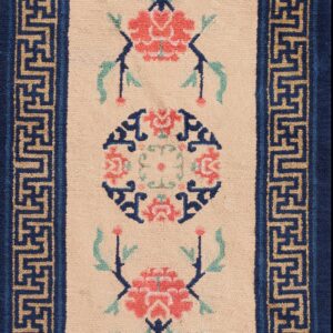 Beige floral runner rug with red and green accents and a navy blue key-patterned border on wood planks.