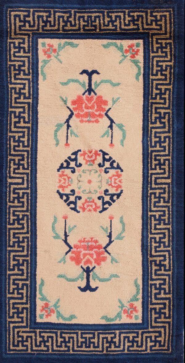 Beige floral runner rug with red and green accents and a navy blue key-patterned border on wood planks.