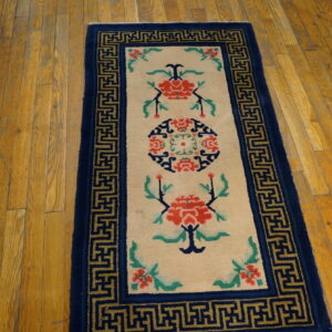 Cream runner rug featuring red flowers and a dark blue Greek key border on distressed hardwood.