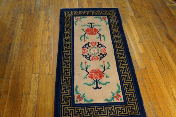 Cream runner rug featuring red flowers and a dark blue greek key border on distressed hardwood.