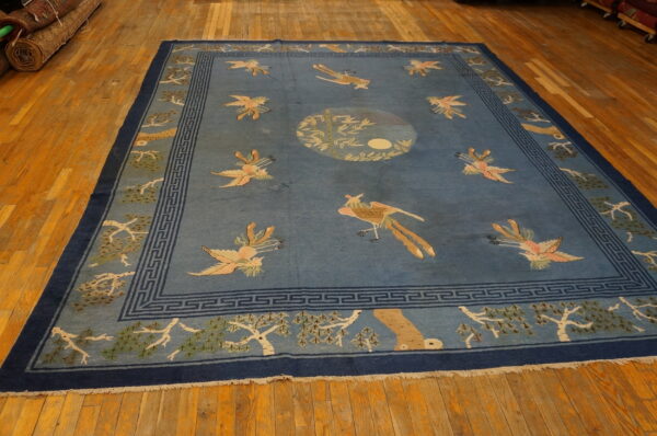 Large blue rug featuring colorful scattered bird patterns, geometric borders, and a central medallion on wood flooring.