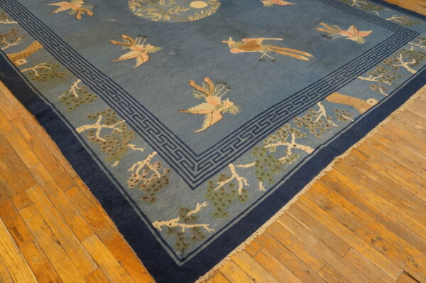 A dusty blue rug with peach birds, stylized trees, and a dark blue key border rests on wood floors.