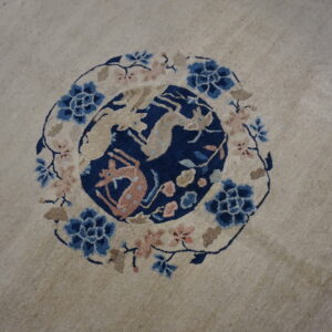 Light rug featuring a central navy blue medallion with beige and pink animal figures and floral border.