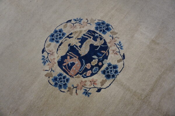Light rug featuring a central navy blue medallion with beige and pink animal figures and floral border.
