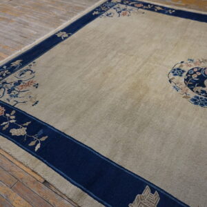 Tan rug with a dark blue border featuring floral patterns and a central medallion on wood floors.