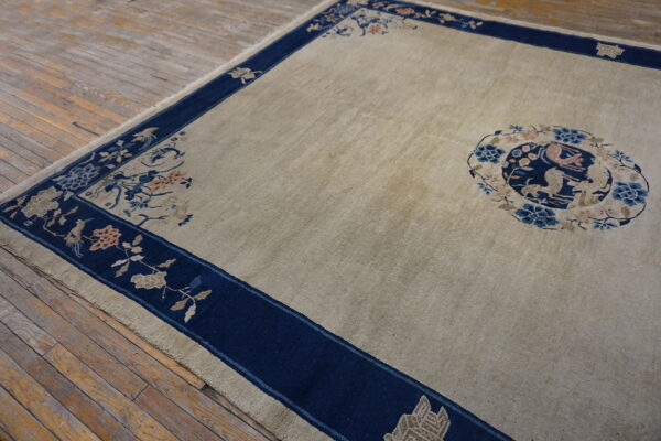 Tan rug with a dark blue border featuring floral patterns and a central medallion on wood floors.