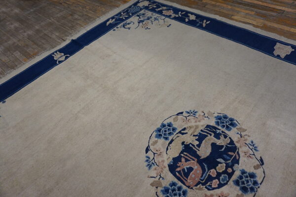 Low pile beige rug featuring a navy border with floral vines and a stylized blue and pink animal medallion.