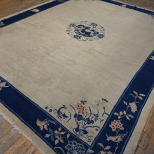 Cream rug with a navy blue border, featuring detailed floral and animal motifs, rests on worn wood planks.