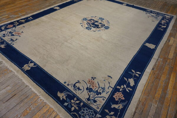 Cream rug with a navy blue border, featuring detailed floral and animal motifs, rests on worn wood planks.