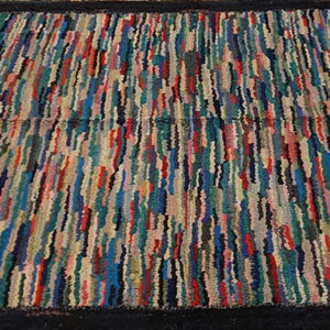 Multicolor striped, high-texture rug with a thick black border lying on rustic wood planks.