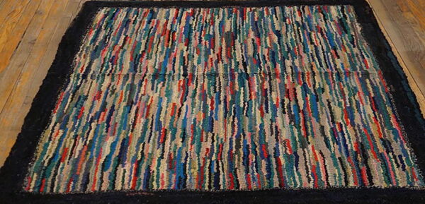 Multicolor striped, high-texture rug with a thick black border lying on rustic wood planks.