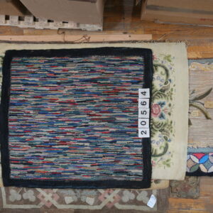 A multicolored striped rug with a dark border lies over a cream rug with floral scrollwork on wood flooring.