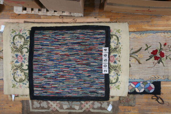 A multicolored striped rug with a dark border lies over a cream rug with floral scrollwork on wood flooring.