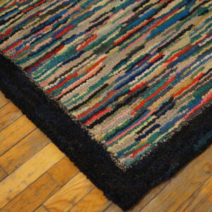 Close-up of a striped, multicolored textured rug with a chunky dark border on wood plank flooring.