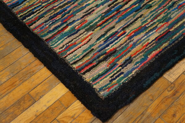 Close-up of a striped, multicolored textured rug with a chunky dark border on wood plank flooring.