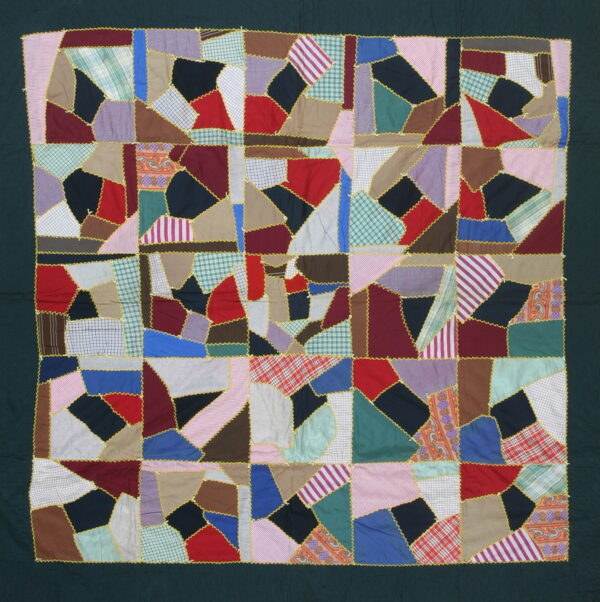 Multi-colored patchwork textile features irregular fabric shapes stitched together with bright yellow zig-zag trim and a dark green border.