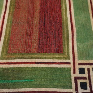 Geometric rug with square blocks in red, green, cream, and black on distressed light wood floor.