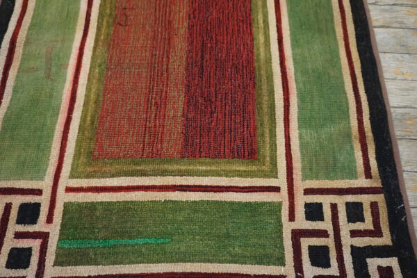 Geometric rug with square blocks in red, green, cream, and black on distressed light wood floor.