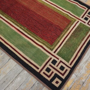 Textured red and green rug with geometric borders rests upon rustic, peeling light wood floorboards.