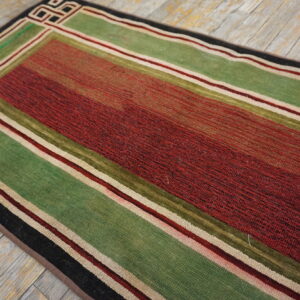 Red and green striped runner rug with thin borders and a corner geometric pattern on rustic wood.