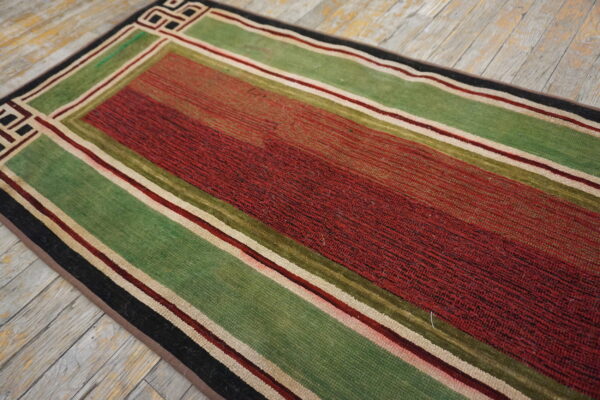 Red and green striped runner rug with thin borders and a corner geometric pattern on rustic wood.