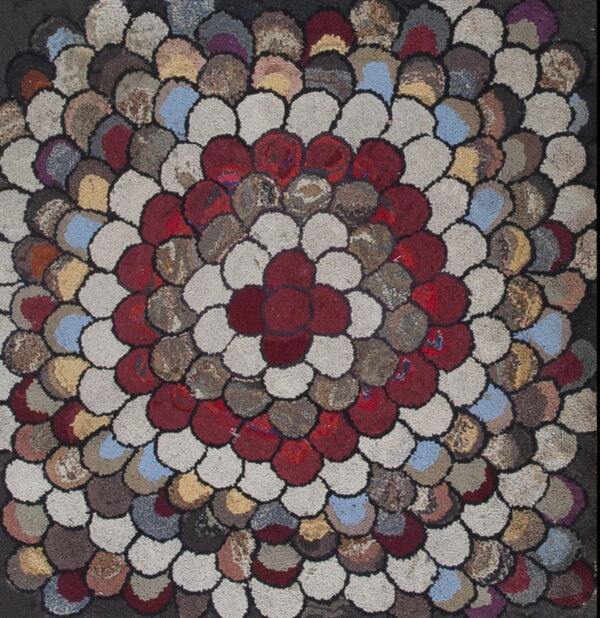 Highly textured rug featuring a central red flower pattern surrounded by rings of scalloped, multicolored patches.