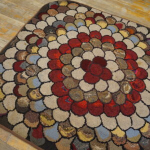 Multicolored rug with chunky, scalloped texture and a central red floral motif sits on distressed wood.