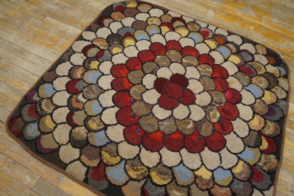 Multicolored rug with chunky, scalloped texture and a central red floral motif sits on distressed wood.