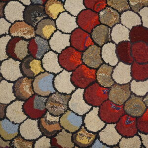 Multicolored hooked rug detail showing irregular rounded shapes in red, beige, brown, and blue.