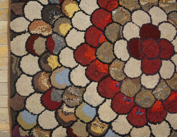 Multicolored hooked rug detail showing irregular rounded shapes in red, beige, brown, and blue.