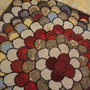 Textured loop rug with multicolored overlapping scale patterns resting on yellow wood planks.