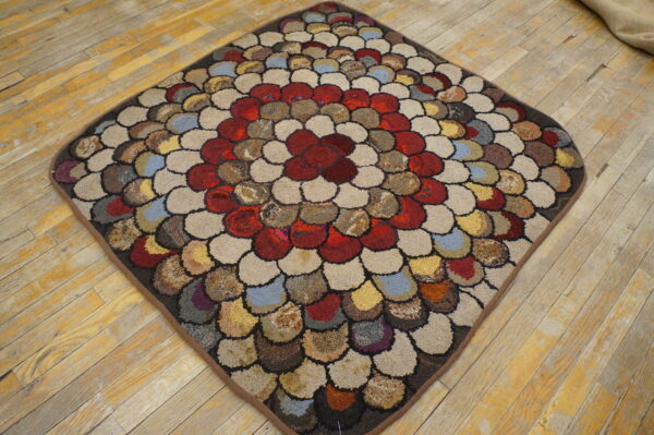Round-edged diamond rug with multicolored hooked scallop patterns rests on rustic wood flooring.