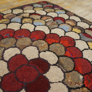 A textured rug displays large, rounded shapes in red, beige, brown, and blue on light wood planks.