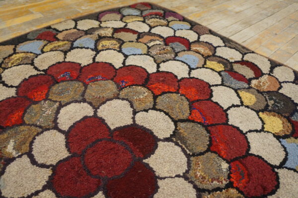 A textured rug displays large, rounded shapes in red, beige, brown, and blue on light wood planks.