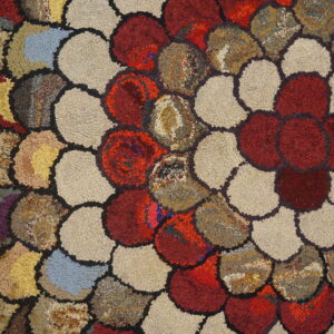 Highly textured rug with large, colorful scalloped shapes in red, beige, and mottled earth tones on a wood floor.