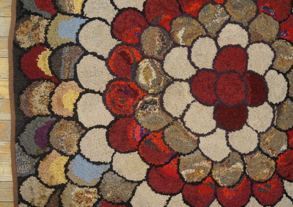 Highly textured rug with large, colorful scalloped shapes in red, beige, and mottled earth tones on a wood floor.