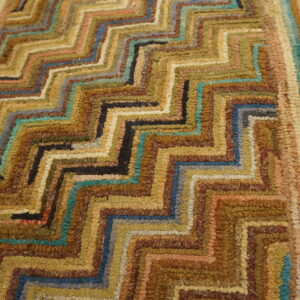 High-texture rug showing concentric zigzag patterns in earthy browns, golds, and bright teal on wood.