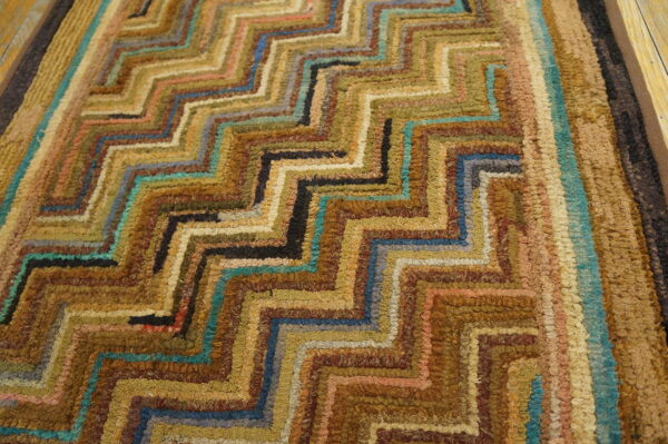 High-texture rug showing concentric zigzag patterns in earthy browns, golds, and bright teal on wood.