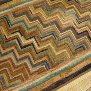 A textured rug with a brown, gold, and teal zigzag pattern rests on light wood plank flooring.