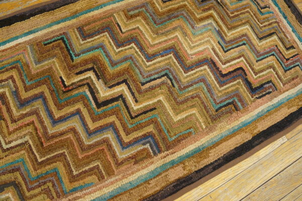 A textured rug with a brown, gold, and teal zigzag pattern rests on light wood plank flooring.