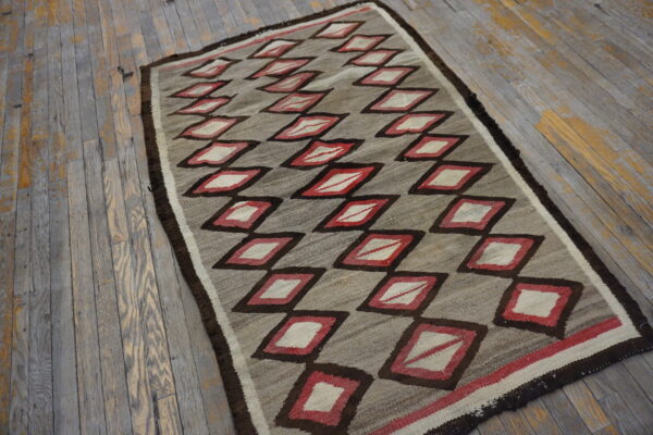 A flatweave rug featuring gray, red, and cream diamonds rests on a distressed gray wood floor.