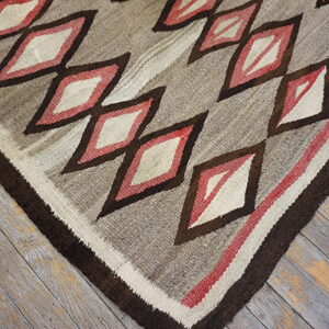 Low-pile rug displaying geometric diamonds in brown, cream, and red tones over weathered wood floor.
