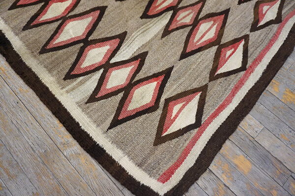 Low-pile rug displaying geometric diamonds in brown, cream, and red tones over weathered wood floor.