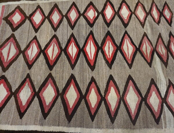 Gray flatweave rug patterned with rows of repeating concentric diamonds in dark brown, red, and cream colors.