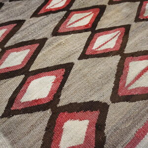 Flatweave rug with a repeating pattern of white and red diamonds outlined in dark brown on a natural tan ground.