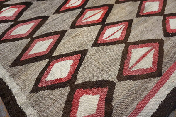Flatweave rug with a repeating pattern of white and red diamonds outlined in dark brown on a natural tan ground.