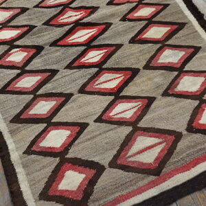 Flatweave rug with dark brown, red, and cream diamond trellis pattern rests on weathered wood floors.