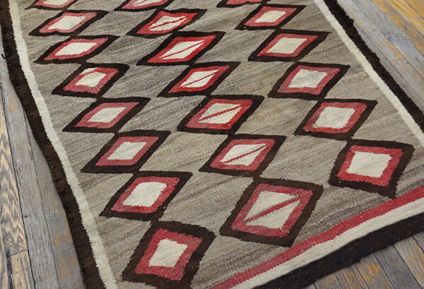 Flatweave rug with dark brown, red, and cream diamond trellis pattern rests on weathered wood floors.